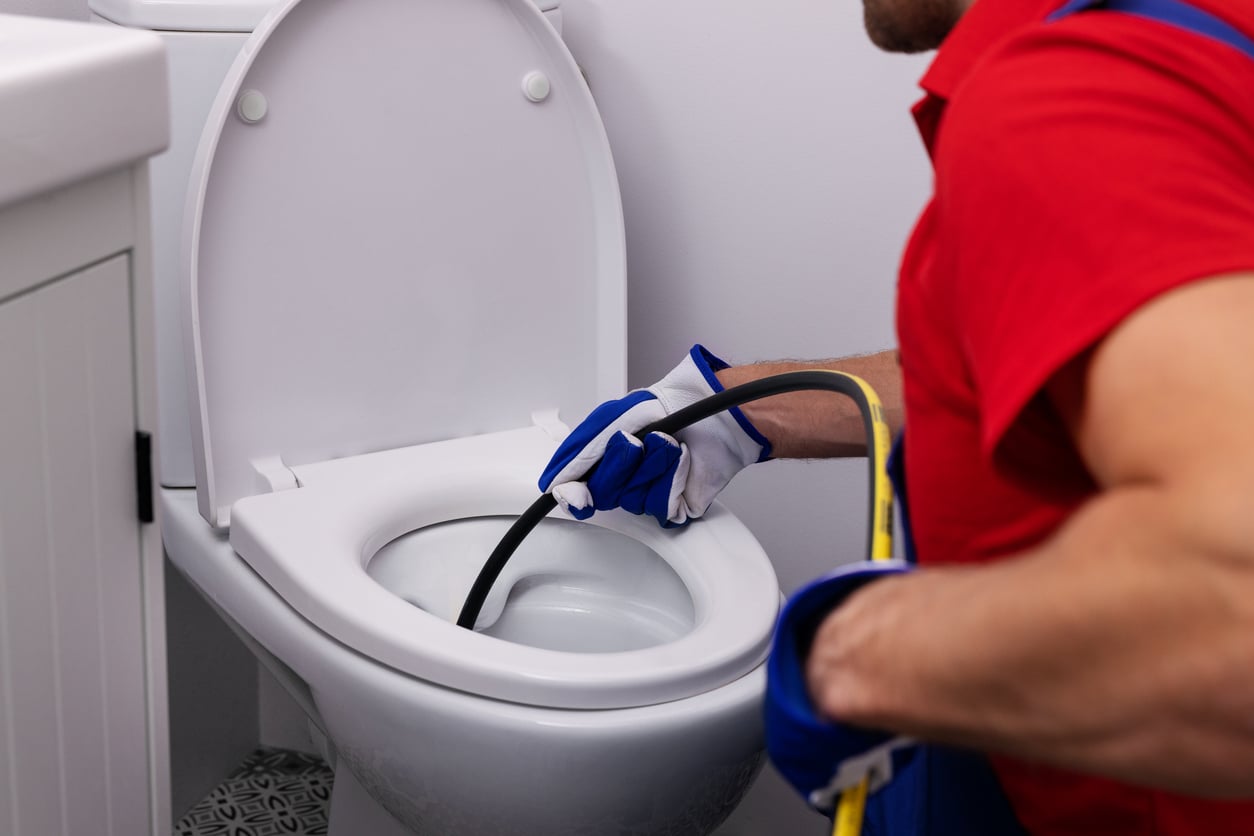 An image of a person feeding a drain snake into a toilet to unclog the drain in a bathroom.